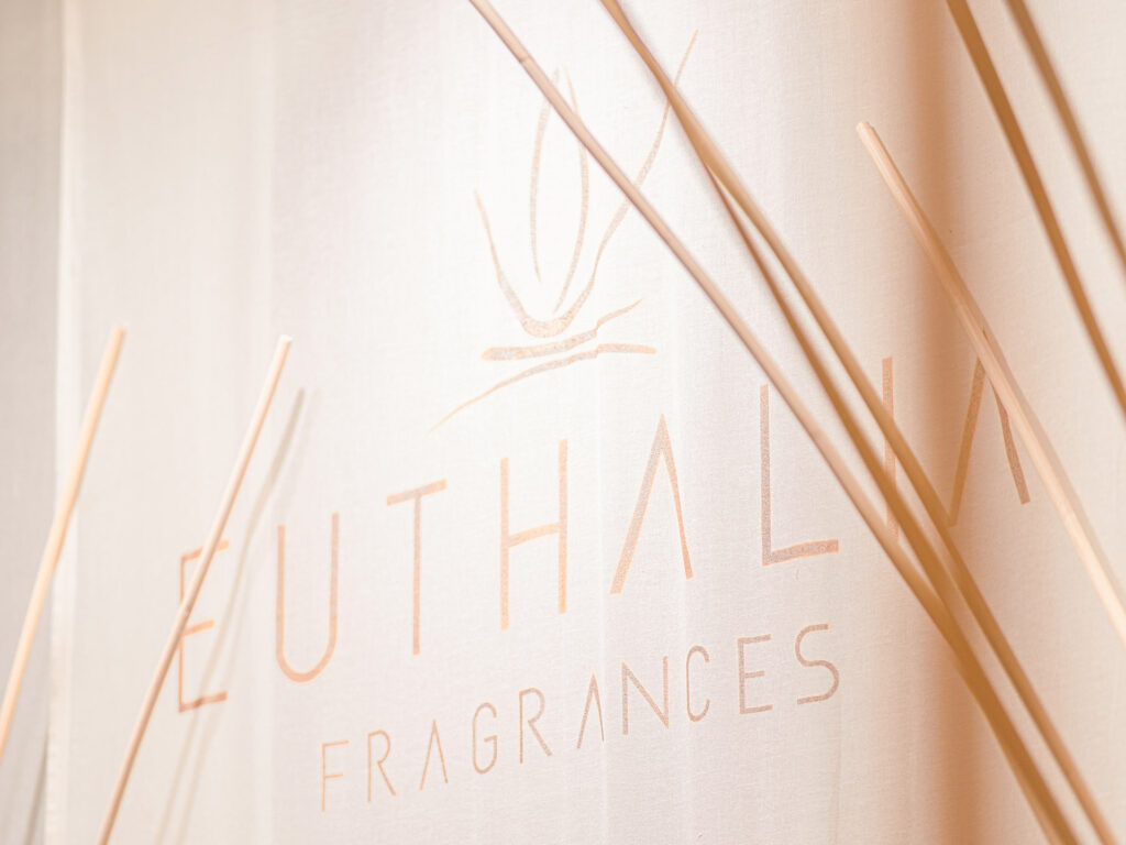 Stand espositivo di Euthalia Fragrances alla fiera Maison & Objet con dettagli in tonalità beige e bastoncini di legno, che rappresentano l'eleganza del design del marchio.